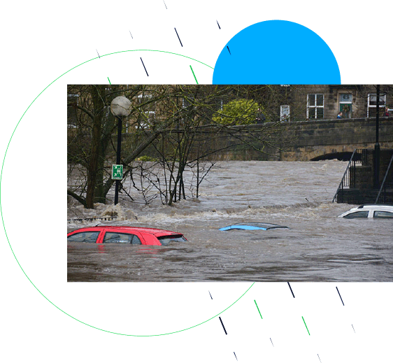 Cars full submerged by flood water. The river has burst its banks and is flowing fast. A bridge can be seen in the distance.