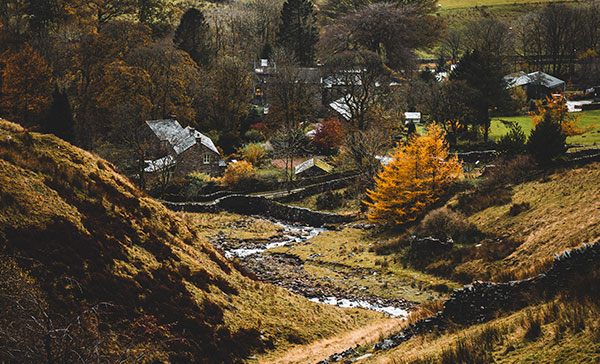 Valleys of Calderdale including a river flowing downstream towards the houses at the bottom of the rolling hills.