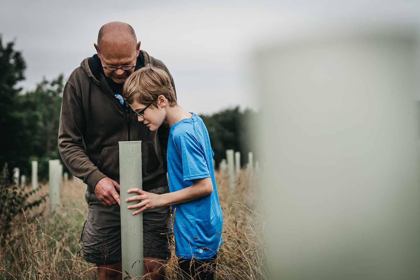 Farmer and his son looking down the protective plastic tube at the tree growing.