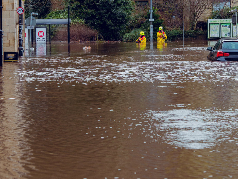 Flooding in Hebden Bridge in 2020 with deep water surrounding cars and emergency workers.