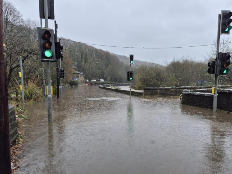 Flooded road and bridge in Calderdale following flooding caused by Storm Bert. Floodwater covering a road and traffic lights during heavy rain.